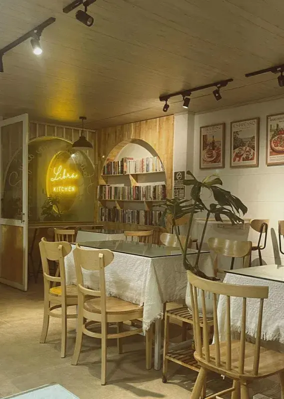 Không gian ngồi Libra Kitchen với tủ sách vòm, biển neon và cây Monstera